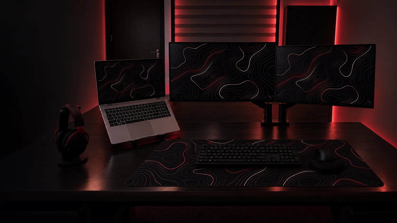 Issa Nijmeh’s workstation: a laptop and three monitors in a dark, red-lit room